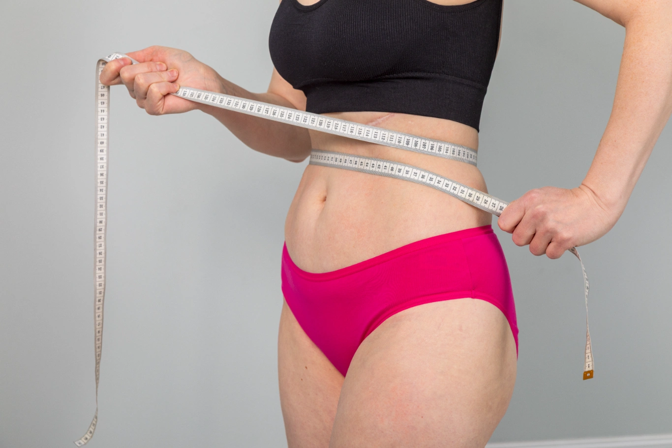 Person measuring waist with tape for body contouring session